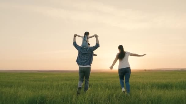 Mam, pap en dochter spelen op het veld, het kind zit op vaders schouders. Gelukkig gezin loopt in het park hand in hand in de zomer bij zonsondergang. Teamwork. Gelukkige gezonde jeugd — Stockvideo