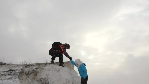 Turističtí horolezci muž a žena natahují ruce k sobě, pomáhají vylézt na vrchol kopce. Cestovatelé jeden po druhém šplhají na útes. Týmová práce obchodníků. Obchodní tým vyhrává.. — Stock fotografie