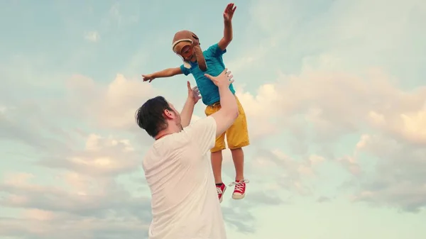 Tata rzuca swojego szczęśliwego syna w błękitne niebo, dziecko jest pilotem, marzy o lataniu. Ojciec i małe dziecko bawią się w parku, śmieją się i przytulają. Szczęśliwa rodzina. Dziecko, rodzic. Dzieciak bawi się z tatą — Zdjęcie stockowe