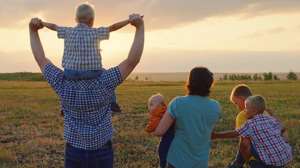 Bonne promenade en famille avec des enfants sur le terrain. Des gens dans le parc. Papa maman, les fils marchent en se tenant la main dans le parc. Bonne vie de famille élever des enfants. En été, les parents, les enfants joyeux se reposent. Vacances en famille — Photo