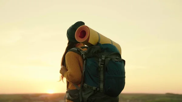 Uma jovem caucasiana ativa com mochila vai em caminhada. Viajante mulher livre caminhando pelo prado no verão. Menina viajante viaja ao longo do topo da colina verde no sol, meditação, ecoturismo, caminhada — Fotografia de Stock