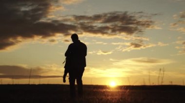 Baba, sevgili bebeğinin elini güneşte tarlada döndürür, bebek uçarken güler. Baba, çocuk ve kız gün batımında parkta oynuyorlar. Sağlıklı bir aile ve çocukluk. Mutlu bir aile. Baba çocuk, oyun parkı.
