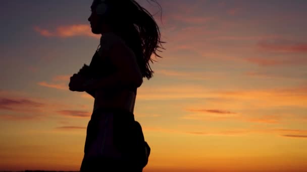 Run and lose weight. Silhouette of free young woman runs in summer in park at sunset, listens to music on headphones. Training jogging. Healthy jogging . Listen to music without Internet, play sports — Stock Video