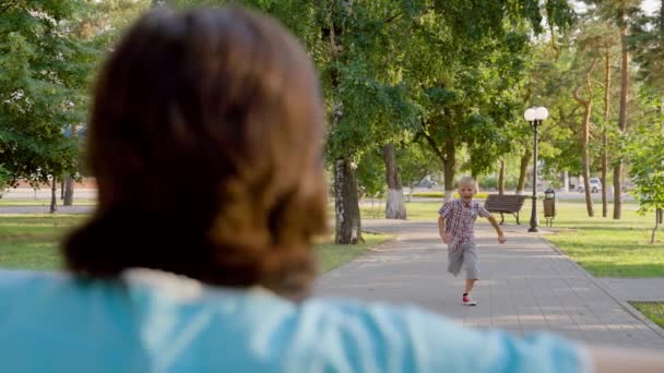 Παιδί μου, ο γιος τρέχει στη μαμά και την αγκαλιάζει στο πάρκο στο δρόμο την άνοιξη. Ευτυχισμένη οικογένεια. Μωρό μου, ανέμελη παιδική ηλικία, χαρούμενο αγόρι που τρέχει στη μητέρα του. Μικρό παιδί έχει τη διασκέδαση παίζοντας το καλοκαίρι στο δρόμο με τους γονείς — Αρχείο Βίντεο