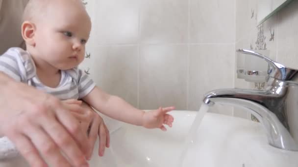 Seorang anak kecil mencuci tangannya dengan ibunya di kamar mandi di atas wastafel. Seorang ibu membantu anaknya mencuci tangan di rumah. Anak itu belajar untuk mencuci tangannya sendiri. Keluarga yang bahagia. Mainkan air dengan anak. — Stok Video