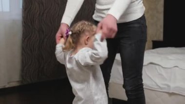 Mutlu aile, çocuk, kız ve baba, el ele tutuşun, zıplayın, yatak odasında dans edin. Baba neşeli bir şekilde tatlı kızı ile aktif bir oyun oynuyor, evde bir çocuk var. Aile tatili, baba izni.