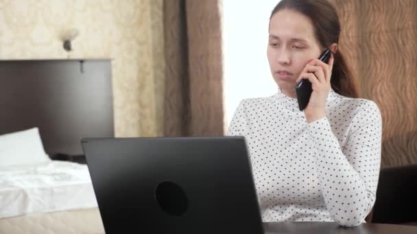 Mujer profesional trabaja con el teléfono móvil de la computadora en casa. Mujer de negocios trabajando en el ordenador portátil en la habitación hablando en el teléfono inteligente. Trabajador independiente que trabaja con computadora portátil moderna y teléfono móvil. — Vídeos de Stock