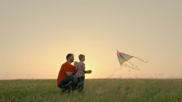 Synowie, chłopcy, tatuś puszczał latawce latem. Rodzina, tata bawi się z dziećmi z latawcem w parku o zachodzie słońca. Ojcze, dzieci wystrzeliwują kolorowy papierowy samolot w niebo. Rodzinny weekend w przyrodzie — Wideo stockowe