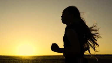 Güneşin peşinden koşmak. Antrenman koşusu. Sağlıklı, güzel bir kız spor yapıyor, kırsalda güneş altında koşuyor. Koşucu kız sahada temiz hava soluyor. Özgür genç kadın gün batımında yaz parkında koşuyor..