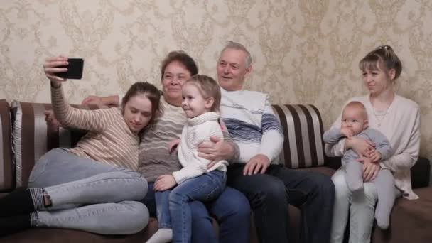 An elderly, mature married couple with their children and grandchildren at home. A happy big family of different ages is photographed on a smartphone, taking selfie together at home. A happy family. — Stock Video