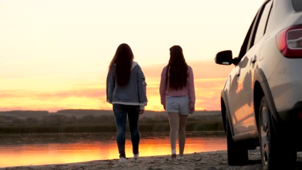 Le ragazze autiste si sono fermate al campeggio. Le donne viaggiatrici libere stanno accanto all'auto sulla spiaggia godendosi il tramonto in un abbraccio al parco e gioendo. Fidanzate stanno godendo viaggio in auto. Viaggio in vacanza in auto, avventura — Video Stock