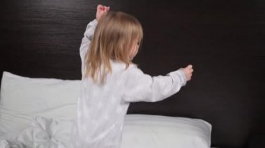 Çocuk sabahları evinde kanepede oynuyor, eğleniyor, şakalaşıyor ve gülümsüyor. Kızım, kızım, bebek yatakta pijamalarıyla zıplıyor ve neşeyle gülüyor. Evde mutlu bir çocukluk geçir. Aile ilişkileri.