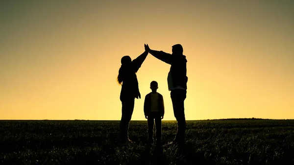 Niños mamá y papá están jugando juntos construyendo casa con sus manos, silueta al atardecer. Felices sueños familiares de su propia casa en el parque en verano bajo el sol. Cuidar a los niños por los padres —  Fotos de Stock