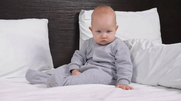 Doce e saudável Filha na cama e observando mamãe e papai. Uma menina se senta em uma cama em um quarto em casa e assiste atentamente a TV. O filho bebé no quarto acordou de manhã.. — Fotografia de Stock