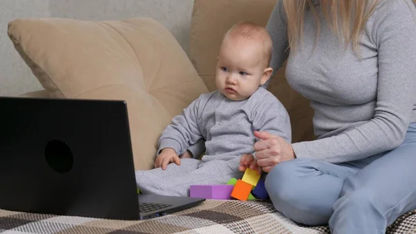 Maternidade moderna. A mãe está a ensinar o filho a usar o computador. Mulher ocupada a trabalhar no portátil com o filho. Trabalho freelancer feminino. Trabalho freelance mãe brinca com seu bebê no sofá. — Fotografia de Stock