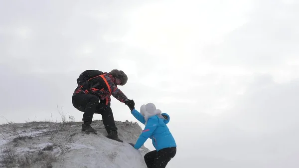 Egyik utazó a másik után mászik fel a sziklára. Az üzletemberek csapatmunka. Turista mászók férfi és nő kinyújtják egymás kezét, segítenek felmászni a dombtetőre. Az üzleti csapat nyert. — Stock Fotó