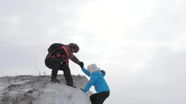 Viajeros uno tras otro suben al acantilado. La gente de negocios trabaja en equipo. Escaladores turísticos hombre y mujer estiran sus manos entre sí, ayudan a subir a la cima de la colina. El equipo de negocios gana —  Fotos de Stock