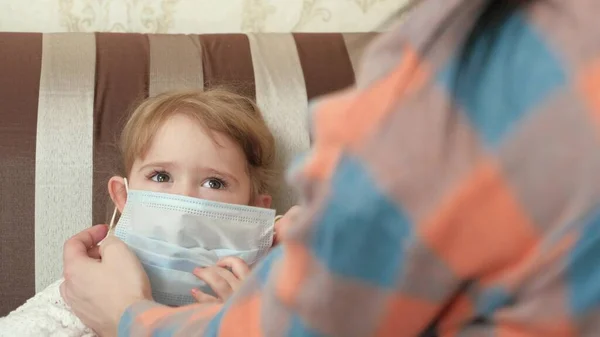 Mam leert hoe ze een medisch masker op moet doen voor haar dochtertje. Familie thuis, preventie van virale ziekten. Moeder laat haar kind zien hoe ze een medisch masker op moet doen. Blijf thuis, mam. Coronavirus of COVID-19. — Stockfoto