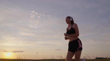 Güneşin peşinden koşmak. Antrenman koşusu. Güzel kız spor yapıyor, kırsalda güneş altında koşuyor. Koşucu kız sahada hava soluyor. Yaz parkında koşan özgür genç bir kadın müzik dinliyor.