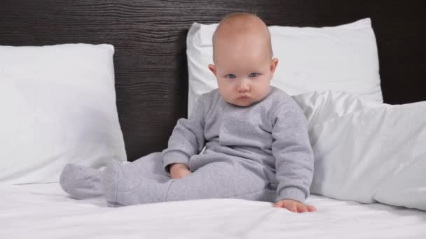 ベッドでお母さんとお父さんを見て甘い健康娘。子供の女の子は自宅のベッドルームでベッドに座って、テレビを注意深く見ています。寝室の赤ん坊の息子は朝起きて. — ストック動画