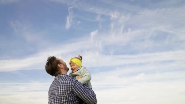 Otec a malé dítě si hrají, smějí se a objímají. Táta vyhazuje šťastnou dceru na modrou oblohu. Šťastná rodina cestuje. Dítě v náručí rodiče. Den volna. Koncept šťastné rodiny — Stock video