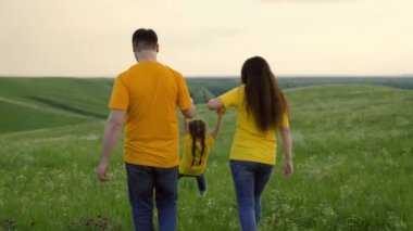 Mutlu aile parkta yürüyor, bahar ve yaz aylarında el ele tutuşuyor. Anne, baba ve kızı tarlada yeşil çimlerde oynuyorlar, mutlu çocuk ebeveynlerinin elini tutuyor ve zıplıyor. Aile günü dışarıda.