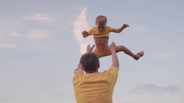 O filho brinca com o pai. O pai atira o filho feliz para o céu azul. Família feliz. Pai e criança brincando no parque, rindo e abraçando juntos. Feliz viagem em família. Bebê está nos braços dos pais — Fotografia de Stock