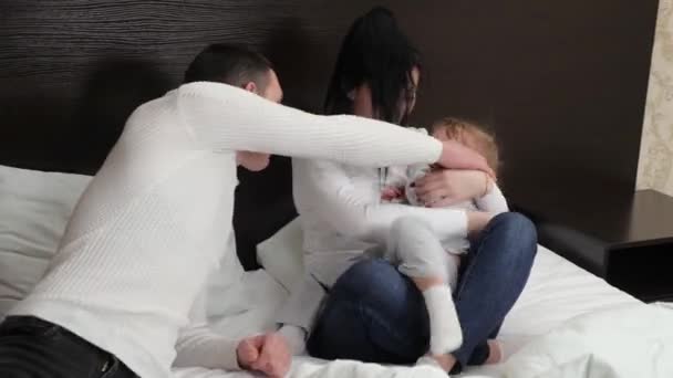 Baby, mom, father are playing on the couch. The child laughs while playing. Happy family, child, daughter, mom, dad, play together in bedroom on the bed. Young parents are playing with small child. — Stock Video