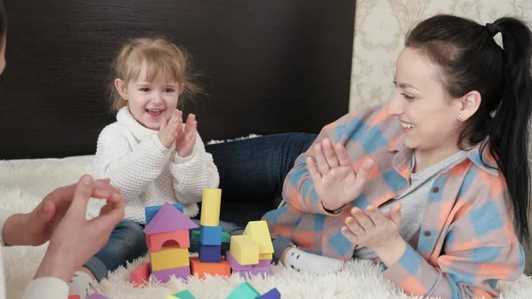 Child, father and mother are playing building family home. Happy family. Educational games for children. Dad, mom, daughter plays with cubes in nursery on bed. Teaching a child through play activities — Stock Photo, Image