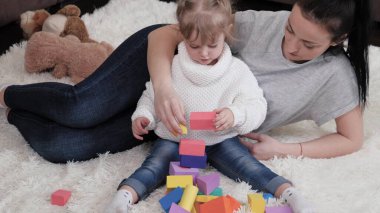 Anne, çocuk yerde bebek odasında küplerle oynuyor. Çocuğa oyun yoluyla öğretmek. Kız ve anne aile evi inşa etme oyunu oynuyorlar. Mutlu bir aile. Çocuklar için eğitici oyunlar. Aile hafta sonu evde