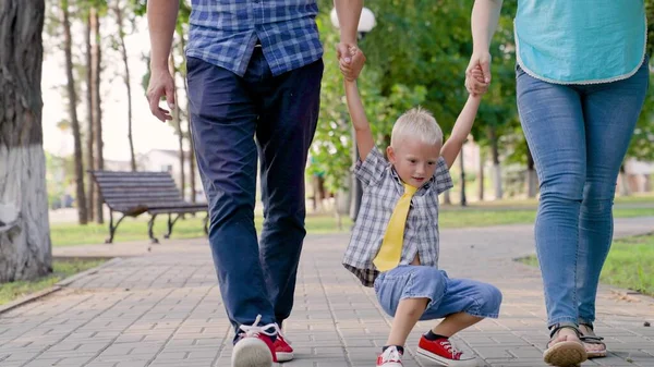 Папа, сын, мама играют в городском парке, счастливый ребенок держится за руки родителей, прыгает. Счастливые семейные прогулки, игры в парке на улице, держась за руки весной, летом. Командная работа. Здоровое детство — стоковое фото