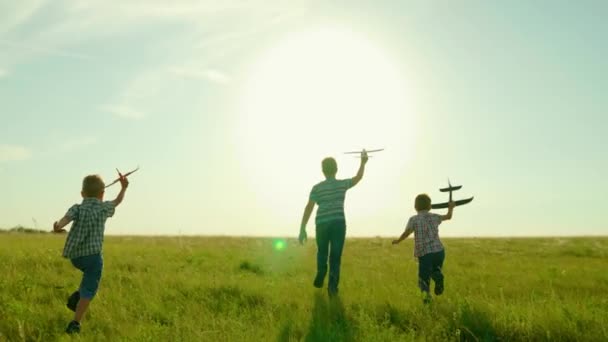 Crianças, meninos correm com avião de brinquedo na mão no campo de verão em raios de pôr do sol. Rapazes sonham voar em grupo. Criança feliz corre no parque, brincando com avião de brinquedo. Crianças despreocupadas com brinquedos brincando ao ar livre — Vídeo de Stock