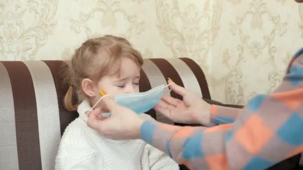 Mère montre à son enfant comment mettre un masque médical. Maman apprend à mettre un masque médical pour sa petite fille. Reste à la maison maman. Coronavirus ou COVID-19. Famille à domicile, prévention des maladies virales — Video