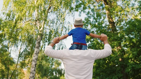 Ο μπαμπάς περπατάει με το γιο του στους ώμους του στο καλοκαιρινό πάρκο. Ευτυχισμένη οικογένεια. Ο πατέρας παίζει με το αγαπημένο του αγόρι, παιδί, μπαμπά και μωρό περπατώντας στο δάσος. Παιδί και γονιός. Οικογενειακό Σαββατοκύριακο στη φύση. Χαρούμενη οικογένεια — Φωτογραφία Αρχείου