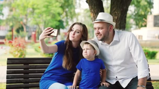 Szczęśliwa mama mama tata syn, małe dziecko są fotografowane przy użyciu nowoczesnego smartfona w parku w lecie. Ojciec maluch matka, rodzice bawią się za pomocą smartfona, selfie lub wideo dzwoniąc razem na zewnątrz — Wideo stockowe
