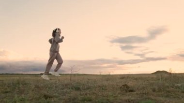 Antrenman koşusu. Özgür genç bir kadın yazın şafak vakti parkta koşar kulaklıkla müzik dinler. Sağlıklı koşu ve açık hava egzersiz konsepti. İnternet olmadan müzik dinlemek ve spor yapmak.