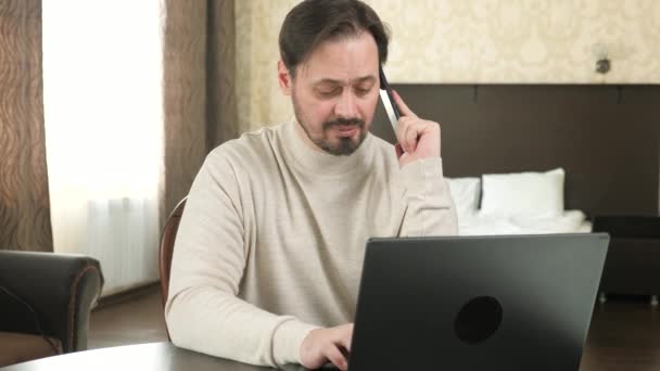 Zakenman, werkend op een laptop, pratend op een smartphone. Freelance werknemer werkt met moderne laptop en mobiele telefoon in de kamer. Mannelijke professionele werken met behulp van een computer en mobiele telefoon in het kantoor, thuis. — Stockvideo