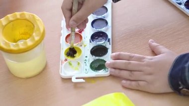 Çocuk bir fırça sarı boya boyar.