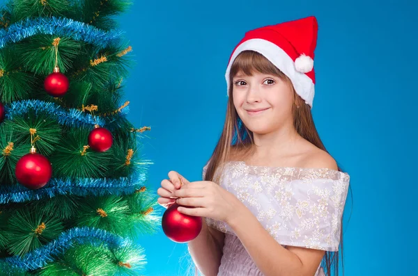 A menina em um gorro vermelho pendura em um abeto com ouropel — Fotografia de Stock