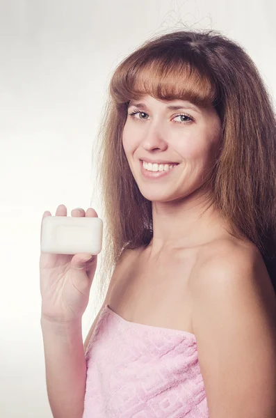 The woman in a towel holds soap in hand and smiles with teeth. — Stock Photo, Image