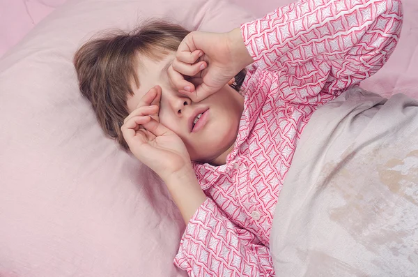 Дівчина в піжамі лежить у ліжку натирає очі — стокове фото
