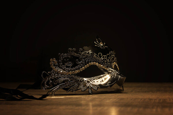 Маска тайны. Портрет венецианской маски на деревянном столе в окружении темноты.
