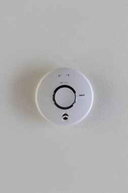 Güvenlik için tavana yapıştırılmış bir duman dedektörünün yakın plan portresi. Yangın alarmı ses çıkararak insanları bir yangına karşı uyarır. Cihaz yuvarlak ve elleri beyaz tavanda..