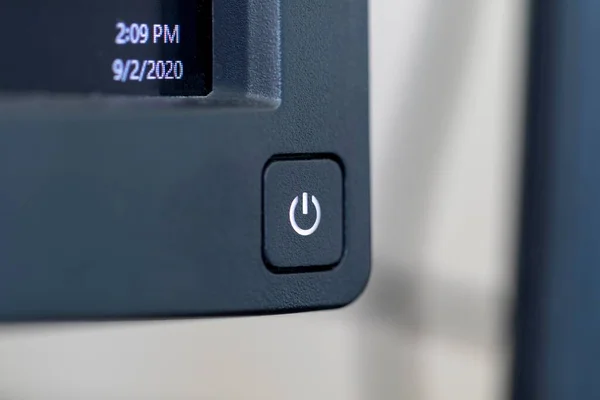A portrait of the on or off button at the corner of a PC monitor ready to be pressed. The computer screen is on, the light in the symbol of the button is on and the screen is showing some information.