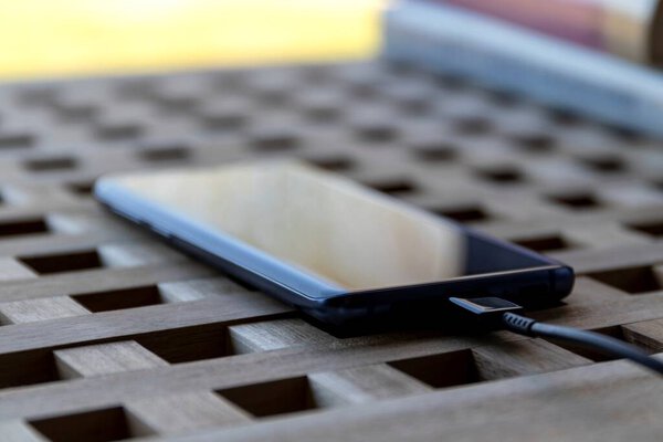 Brecht/Belgium - April 1 2020: A portrait of a smartphone with a USB cable in its port lying on a table. It is either connected to something like a computer to transfer data or charging.