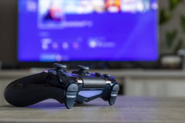 BRECHT, BELGIUM 28 Mart 2019 Bir PS4 kontrolörünün portresi, televizyonun önünde açılır. Televizyon bulanıklaşıyor ve Playstation ana ekranını görüntülüyor.