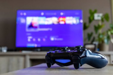 BRECHT, BELGIUM 28 Mart 2019 Bir PS4 kontrolörünün portresi, televizyonun önünde açılır. Televizyon bulanıklaşıyor ve Playstation ana ekranını görüntülüyor.