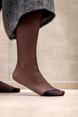 Seksi siyah külotlu çorabıyla eteğini kaldıran bir kızın başucunda duran bir ayağın yakın plan portresi. Naylon ayak parmaklarıyla desteklenir..