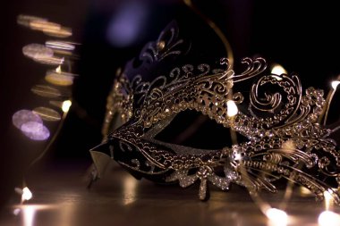 Işıklarla çevrili ahşap bir masanın üzerindeki gizemli bir maskenin portresi. Venedik maskeli baloda birinin kimliğini saklamak için mükemmeldir..