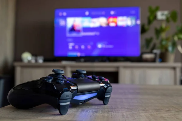 2019年3月28日在电视电视机前的一张木制桌子上的索尼Playstation 4控制器的肖像 显示了Ps4的主屏幕 — 图库照片